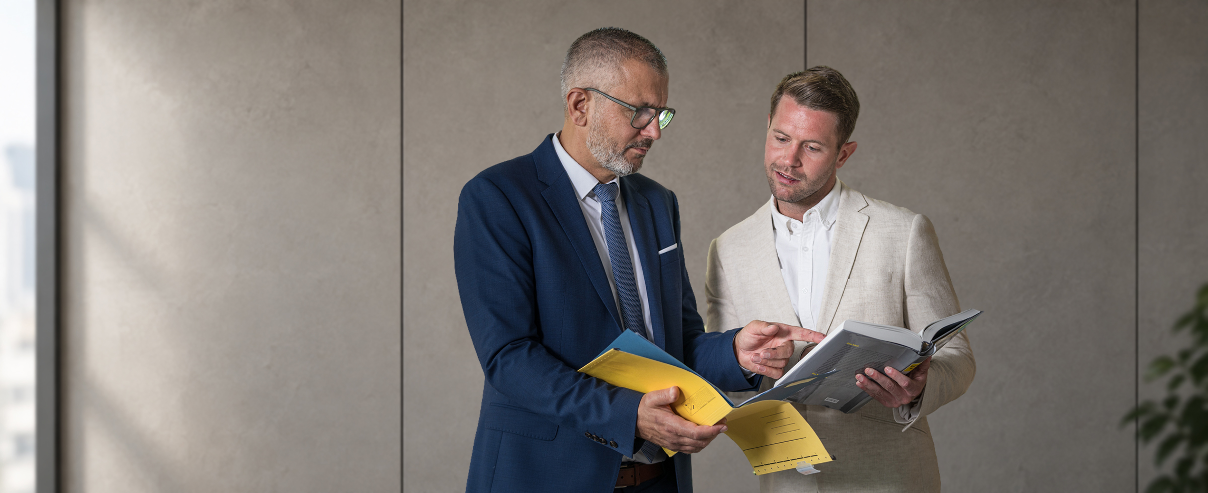 Dr. Siegfried Zachhuber und ein Gesprächspartner besprechen Unterlagen in einem aufgeschlagenen Buch.
